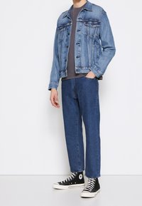 Hellblaue Jeansjacke mit zwei vorderen Taschen, kombiniert mit dunkelblauen geraden Jeans und schwarzen High-Top-Sneakern.