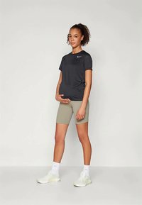 T-shirt noir à manches courtes Nike, shorts de cyclisme beiges et baskets blanches. Le t-shirt a un logo sur la poitrine. Matériau lisse et ajusté.