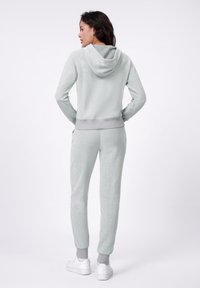 Lichtgrijze hoodie en joggers van textuurstof, met een capuchon en elastische manchetten, gecombineerd met witte sneakers.