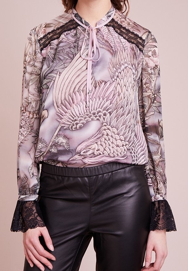 Blusa transparente de manga larga con estampado de pájaros, puños de encaje y detalle de lazo en el cuello, combinada con pantalones de cuero negros.