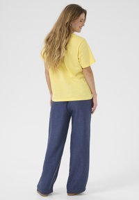 Kollane puuvillane T-särk ümmarguse kaelusega, koos laia lõikega tumeda sinise tekstureeritud pükstega. Lihtne disain, mugav lõige.
