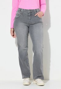 Jeans in denim grigio con vestibilità rilassata, caratterizzati da un cinturino alto, tasche frontali e una texture liscia. Abbinati a scarpe di colore chiaro.