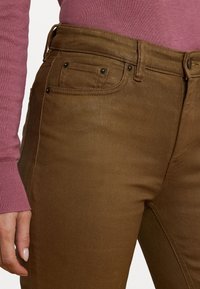 Bruna denimbyxor med en figurnära design, med framfickor, subtil textur och en slät yta. Bärs tillsammans med en rosa stickad tröja.