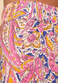 Tessuto a fantasia floreale colorato con sfumature di rosa, giallo e blu. Presenta una cerniera bianca e un dettaglio di vita elastica.