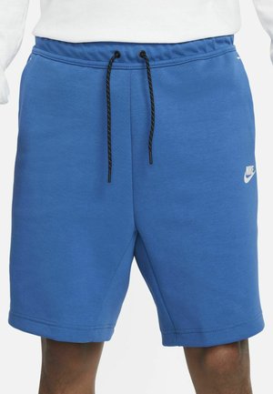 Niebieskie bawełniane szorty z elastycznym paskiem do regulacji, z białym logo Nike na dolnej części nogawki i gładką fakturą.