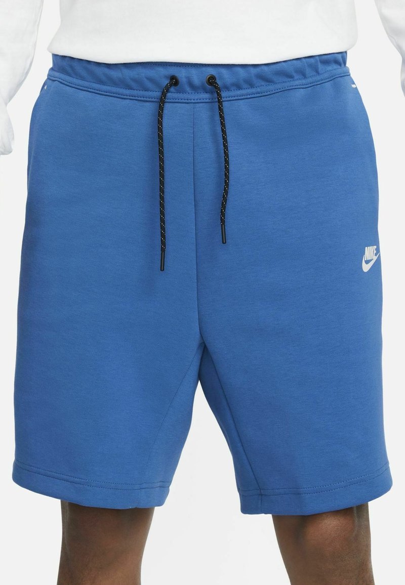Shorts en coton bleu avec une taille à cordon de serrage, arborant un logo Nike blanc sur la jambe inférieure et une texture lisse.