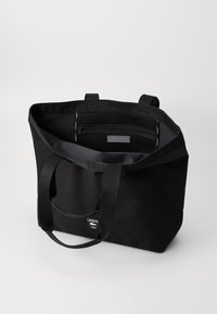 Borsa tote nera Lacoste con doppio manico, tasca frontale e scomparto in rete con zip all'interno, mostrata su uno sfondo neutro.