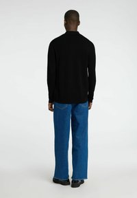 Svart strikket genser og blå vide jeans. Genseren har krage, mens jeansene har en klassisk fem-lomme-design og lys søm.