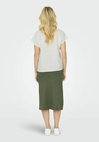 Hvid kortærmet bluse parret med en lang grøn strikket nederdel. Sættet suppleres af hvide sneakers. Stoffet virker let og tekstureret.