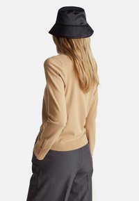 Jasnobrązowy sweter dzianinowy z prążkowanym dołem i mankietami, w połączeniu z szarymi szerokimi spodniami. Czarna czapka typu bucket dopełnia strój.