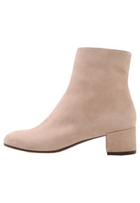 Botín de ante beige hasta el tobillo con puntera redondeada y tacón cuadrado. Textura suave y diseño minimalista, adecuado para varios atuendos.