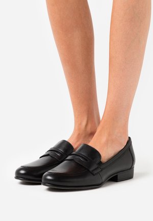 Mocassins en cuir noir avec un bout arrondi et un design piqué, présentant une large sangle sur le cou-de-pied et un petit talon bloc.