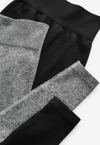 Fekete és szürke leggings halmozva; texturált szürke anyag ribbed fekete derékpánttal. Simább fekete anyag az alsó részen.