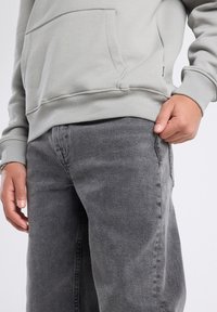 Lichtgrijze hoodie met een voorzak en geribbelde manchetten, gecombineerd met donkergrijze jeans met een rechte pijp en naaddetails.