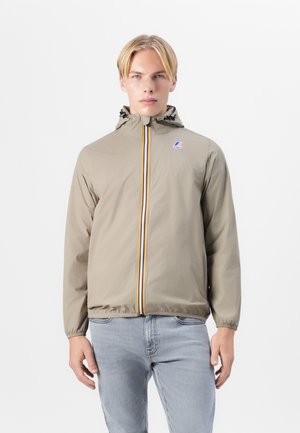 Lichtbeige windbreakerjack met een capuchon, voorzien van een rits aan de voorkant met gele, oranje en blauwe strepen en elastische manchetten.