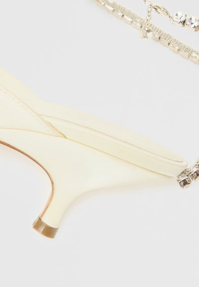 Yellow satin high-heeled shoe with a pointed toe, featuring a decorative silver chain with rhinestones along the ankle strap.