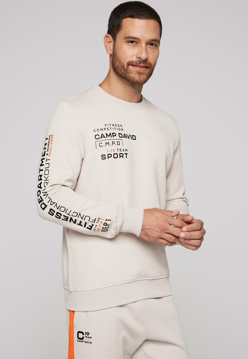 Lys grå sweatshirt lavet af blødt stof, med grafisk tekst i sort og orange, samt ribbede manchetter og talje.