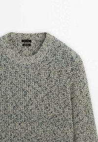 Pull en maille texturée de couleur grise avec des éclats de marron et de bleu. Il présente un col rond et des bords côtelés aux poignets et à l'ourlet.