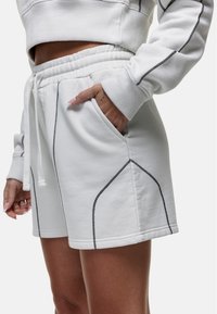 Witte katoenen shorts met een elastische tailleband en trekkoord, voorzien van contrasterende zwarte stiksels en zijzakken, met een gladde textuur.