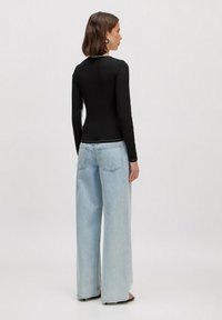 Zwarte lange mouwen top met een aansluitend design, gecombineerd met lichtblauwe wijde jeans. De outfit heeft eenvoudige stiksels en een ontspannen pasvorm.