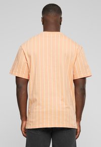 T-shirt à manches courtes en pêche, avec des rayures verticales blanches. Coupe classique avec un col rond et une coupe décontractée. Matière en coton souple.