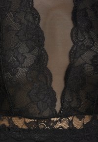 Lencería negra de encaje con detalles de malla transparente. Presenta patrones florales y bordes ondulados a lo largo del escote y el dobladillo. Diseño texturizado y delicado.
