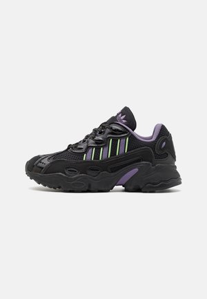 Czarno-fioletowe buty sportowe Adidas z zielonymi paskami, cholewką z siateczki i skóry, zapinane na sznurowadła z przodu oraz grubą, ukształtowaną gumową podeszwą.