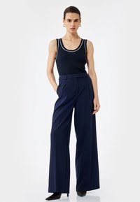 Navyblaue gerippte Tanktop mit weißem Saum, kombiniert mit hoch taillierten, weit geschnittenen Hosen aus einem glatten Stoff. Tragen mit schwarzen High Heels.
