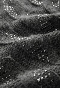 Tissu tricoté gris foncé avec des motifs en relief texturés et de petits sequins carrés brillants éparpillés cousus sur la surface.