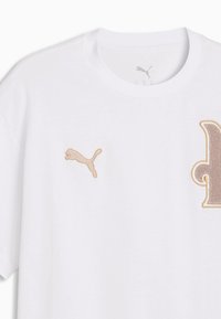 T-shirt blanc Puma avec un logo Puma brodé beige sur la poitrine gauche et une grande lettre « p » texturée beige sur la poitrine droite.
