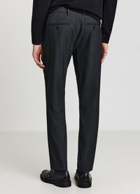 Pantaloni slim fit grigio scuro realizzati in tessuto strutturato, dotati di due tasche posteriori con chiusura a bottone. Indossati con scarpe nere.