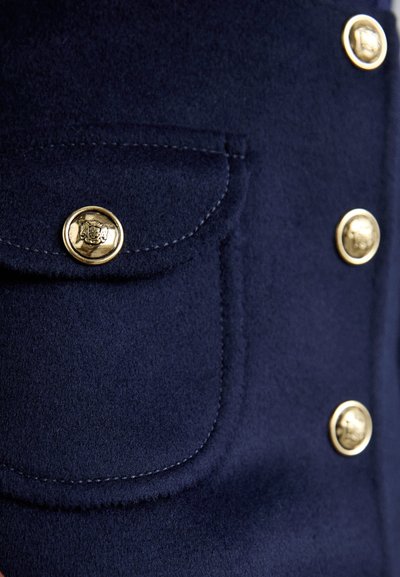 Navy wool-blend jacket featuring a chest pocket with a gold button closure, gold buttons down the front, and fine stitching details.