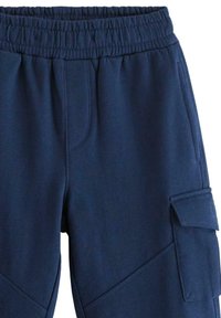 Marineblaue Trainingshose mit einem elastischen Bund, ausgestattet mit zwei Seitentaschen und einer Cargo-Tasche am Oberschenkel. Glatte Textur und lässiges Design.