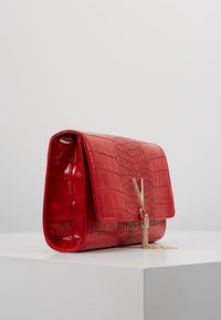 Borsa a tracolla rossa in ecopelle con motivo coccodrillo e chiusura in metallo dorato con dettagli in catena. Forma rettangolare strutturata, texture liscia.