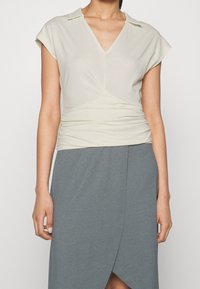 Light beige top with cap sleeves, v-neck, and gathered detailing at the waist, paired with a gray wrap skirt featuring a diagonal hem.