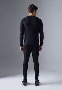 Cămașă neagră cu mâneci lungi și sleevuri raglan, împreună cu leggings ajustați asortați, realizate dintr-un material neted și elastic. Purtați cu pantofi sport negri.