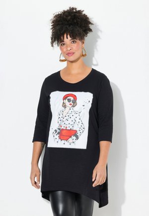 Tunique noire avec une courte manche raglan, ornée d'une illustration imprimée d'une femme en pois, portant un béret rouge et un sac à main rouge.
