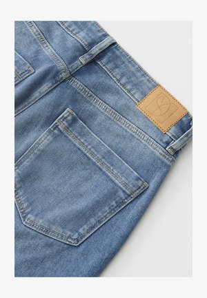 Back view of light blue denim jeans showing right back pocket, belt loop, stitching details, and a tan leather brand label on waistband.