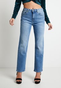 Ljusblå jeans med hög midja och raka ben, fem fickor och klassisk denimstruktur, kombinerade med svarta platåsandaler.