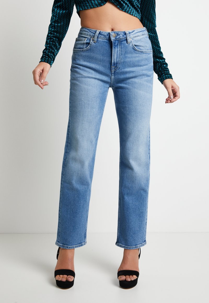 Ljusblå jeans med hög midja och raka ben, fem fickor och klassisk denimstruktur, kombinerade med svarta platåsandaler.