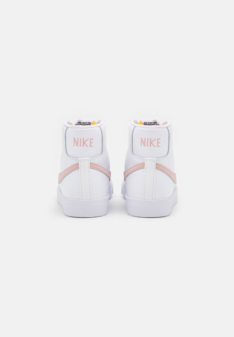 Zapatillas altas blancas con acentos rosas y la marca "NIKE" en el talón. Presentan un upper de cuero y una suela de goma texturizada.