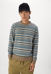 Pulover tricotat cu un model geometric în nuanțe de albastru, bej și alb, cu manșete și tiv cu nervuri, și guler rotund. Asortat cu pantaloni khaki.