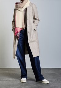 Manteau gris clair en mélange de laine avec une coupe ajustée, écharpe à carreaux crème et rose, jean bleu foncé coupe décontractée, et baskets blanches.