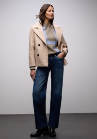 Beżowy dwurzędowy płaszcz z czarnymi guzikami, jasnoniebieski i beżowy sweter w wzory, ciemne, szerokie spodnie jeansowe oraz czarne botki na obcasie.