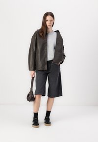 Tume nahkjakki, hall kapuutsiga särk, mustad denim-lühikesed püksid ja mustad jalatsid, millel on heledad tallad. Aksessuaarideks on väike pruun kott.