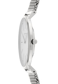 Montre en acier inoxydable argenté avec un boîtier rond slim, un cadran blanc minimaliste et un bracelet en maille. Présente une couronne sur le côté et des repères d'heure discrets.