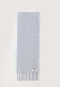 Écharpe bleu clair en tissu doux, avec une texture unie, terminée par des franges. Une petite étiquette de marque est présente à un bord.