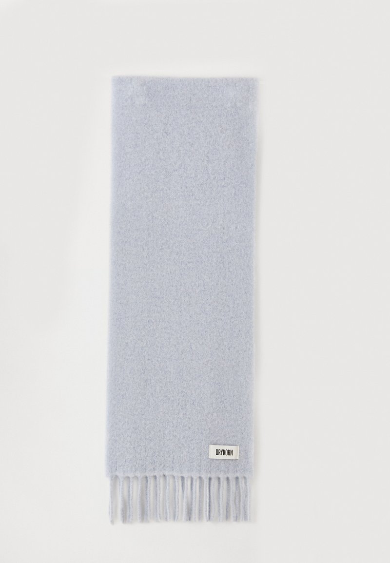 Écharpe bleu clair en tissu doux, avec une texture unie, terminée par des franges. Une petite étiquette de marque est présente à un bord.