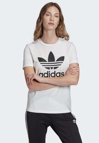 Witte katoenen t-shirt met een groot zwart Adidas trefoil logo en tekst. Korte mouwen en ronde halslijn; zachte textuur.