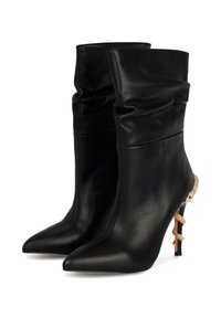 Stivali ankle in pelle nera con punta appuntita e design svasato. Presentano un dettaglio dorato vicino al tallone. Tacco a stiletto alto.